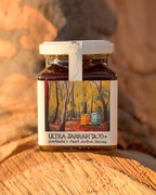 A jar of Ultra Jarrah TA70+ honey placed on a wooden surface with a scenic label depicting a forest.