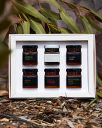 Set of six small jars with labels in a white box, surrounded by natural elements.