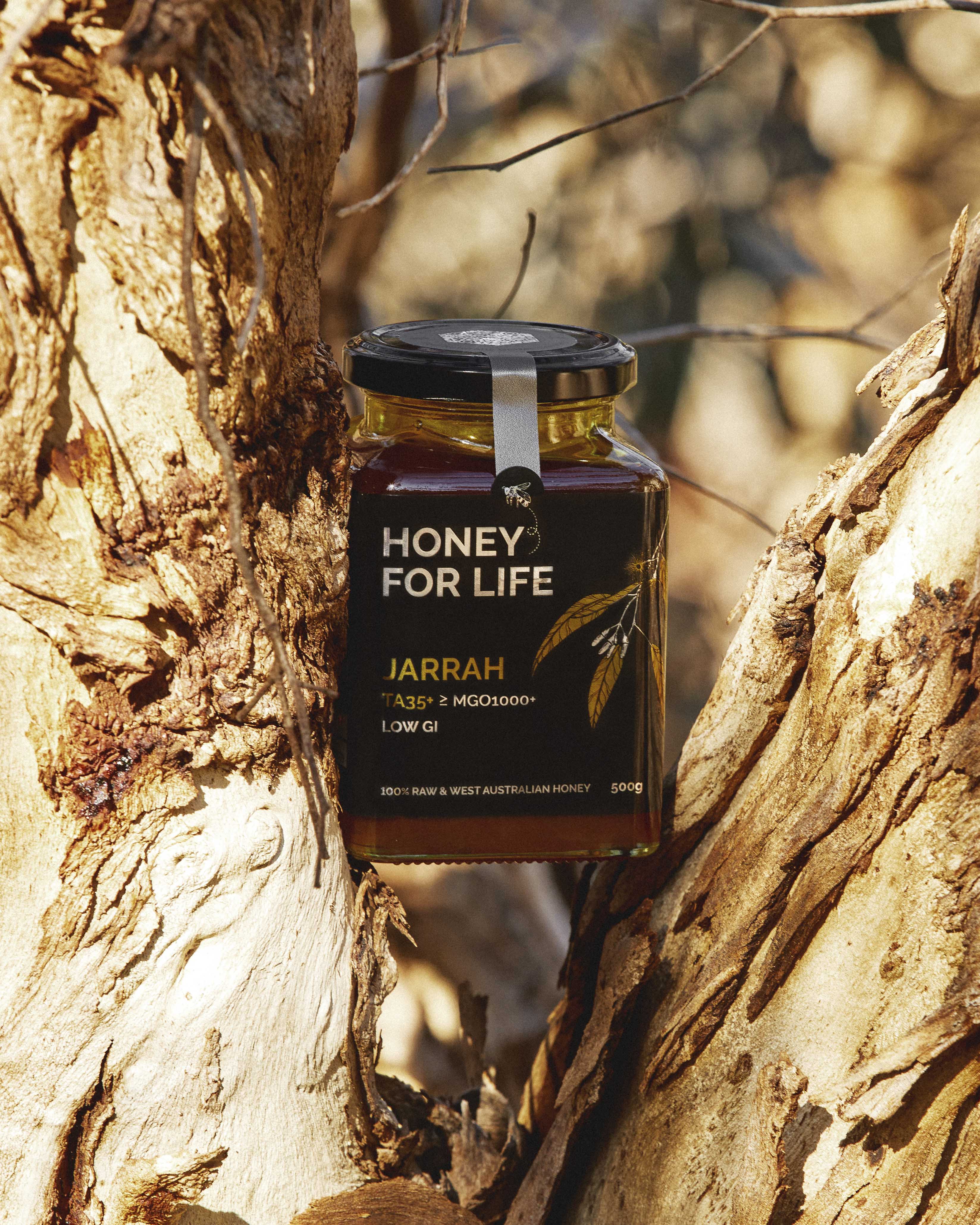 Jar of 'Honey for Life' jarrah honey against a tree bark background