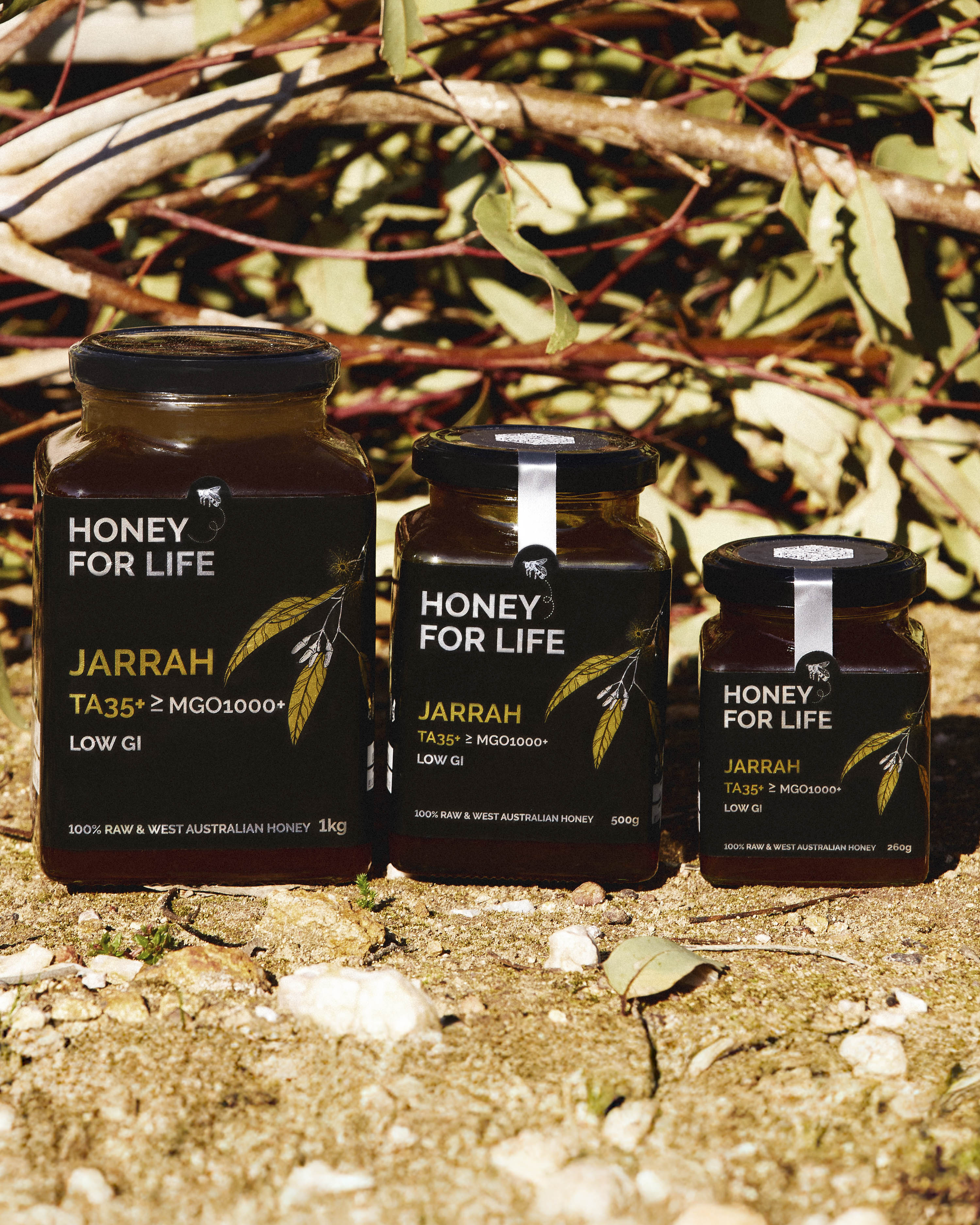Three jars of 'Honey for Life' jarrah honey on a natural background with leaves and branches.