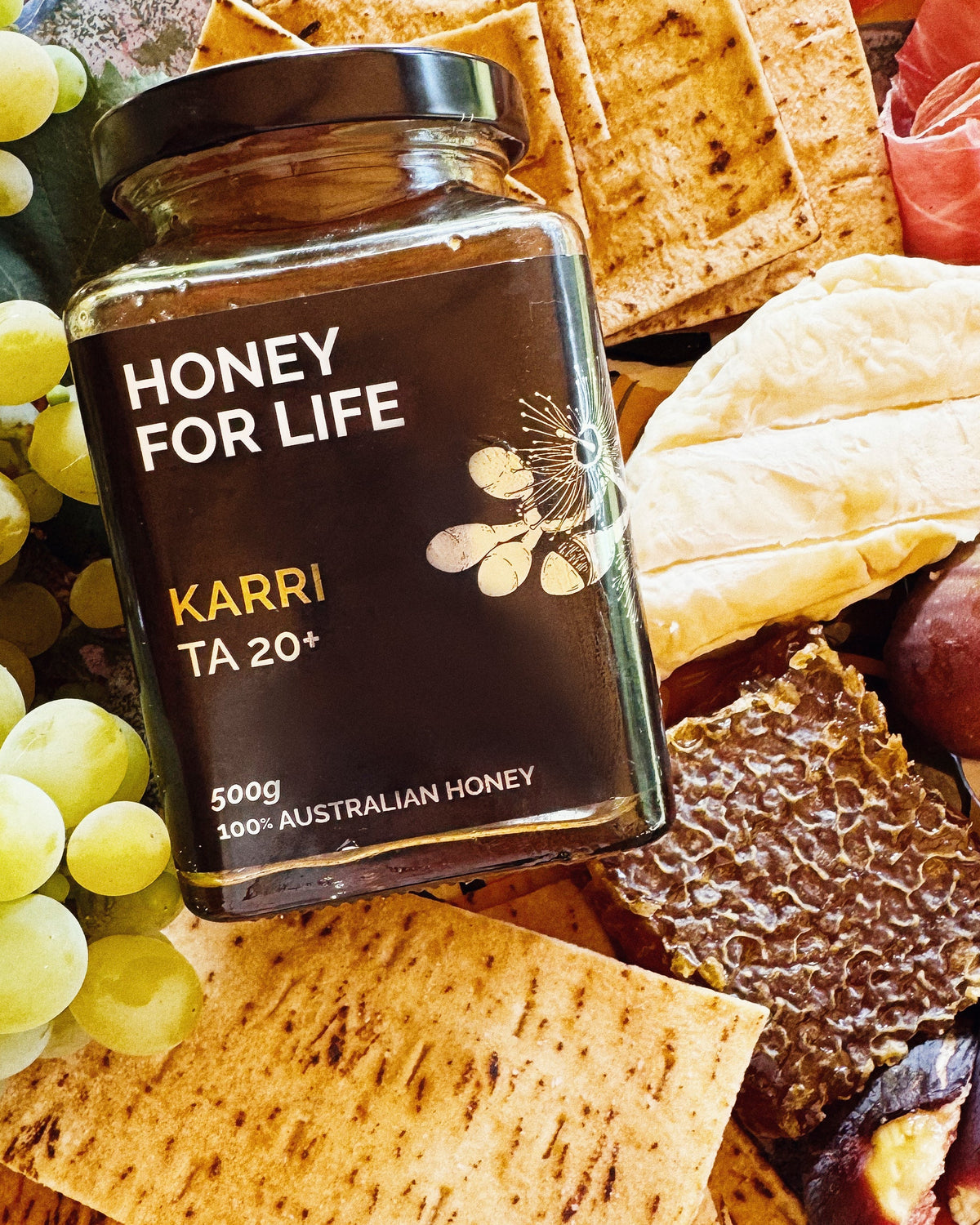 A jar of ACTIVE KARRI HONEY TA20+ placed on a table with various food items around it, indicating a setting for honey tasting.