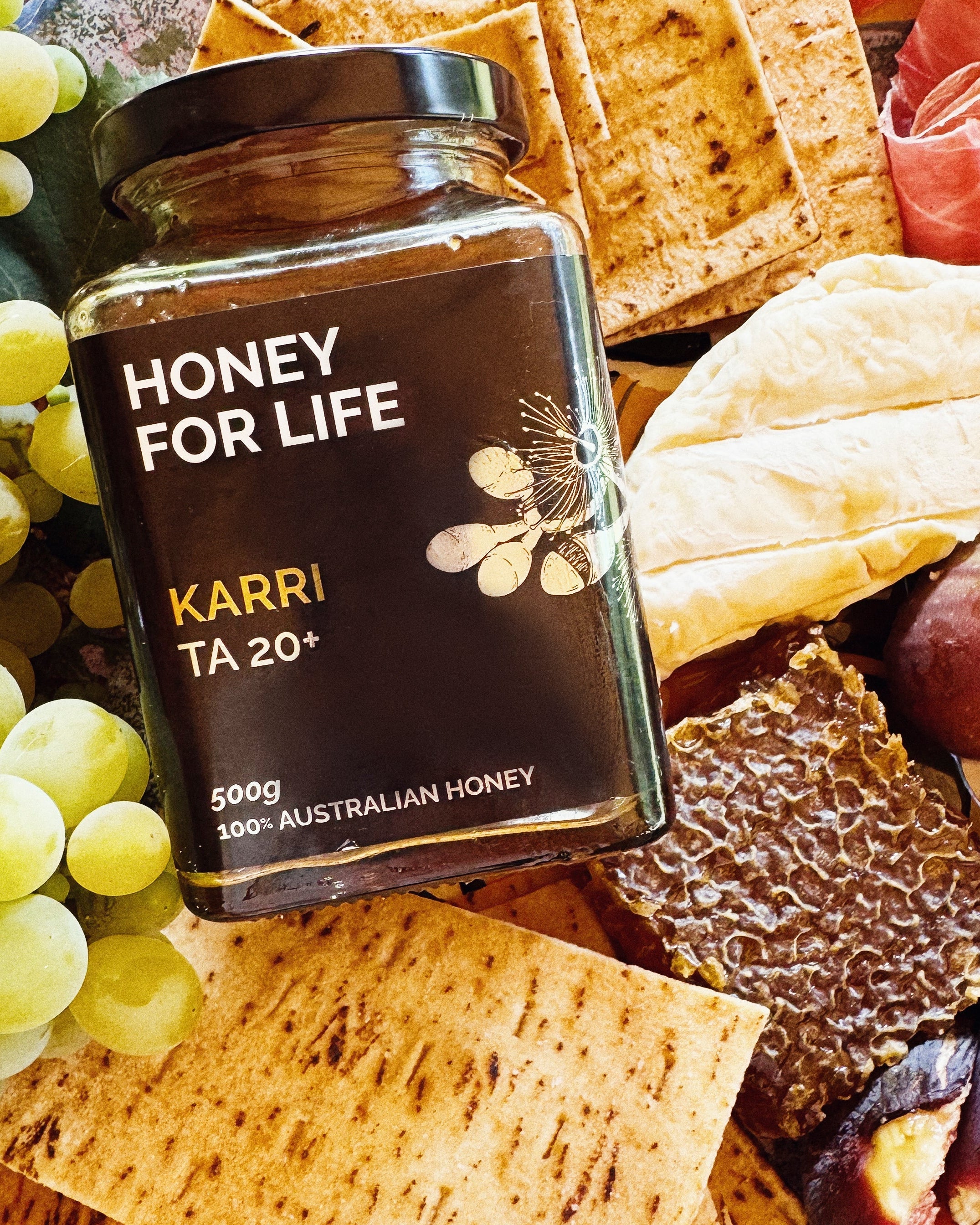 A jar of ACTIVE KARRI HONEY TA20+ placed on a table with various food items around it, indicating a setting for honey tasting.