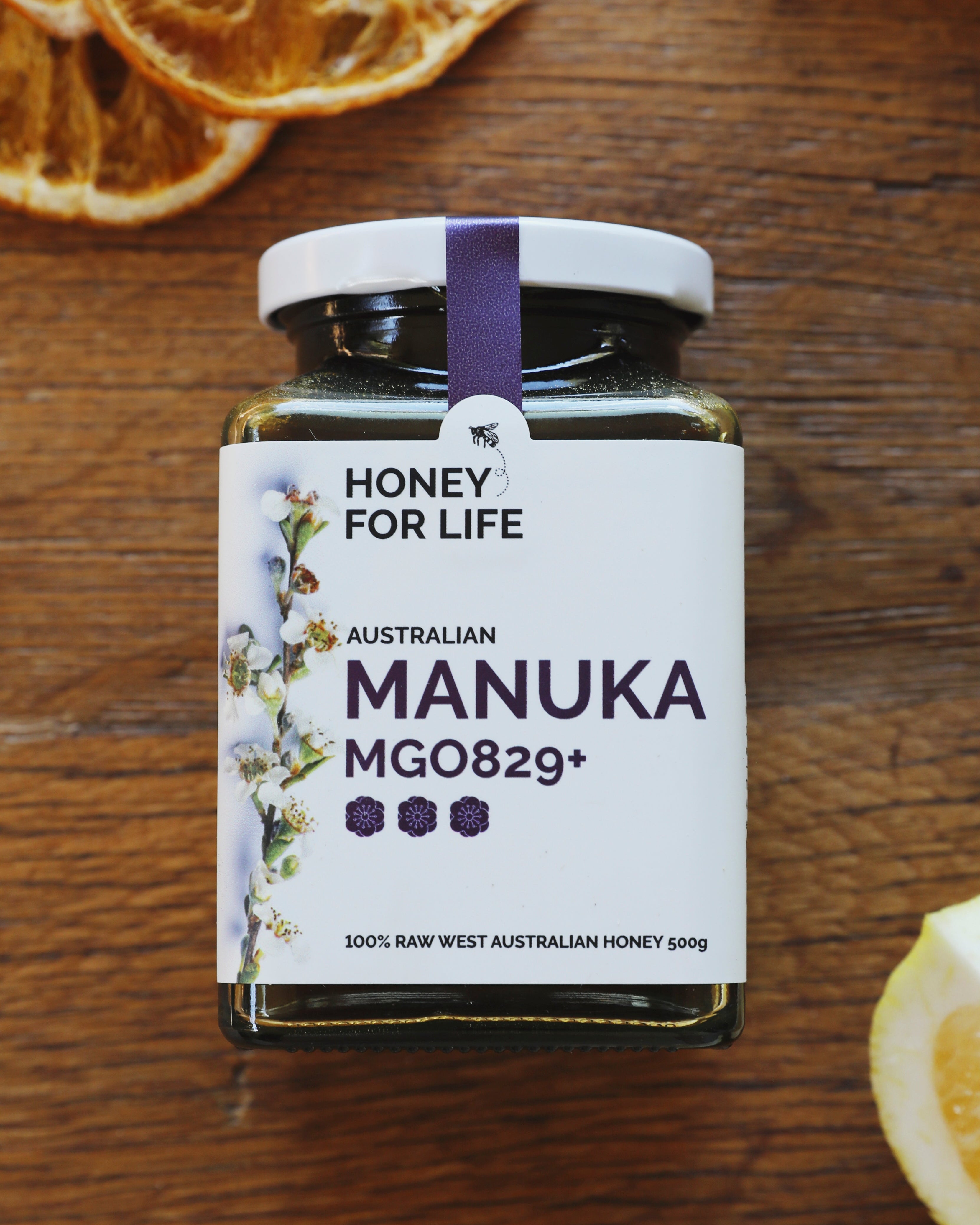 Jar of 'Honey for Life' Australian Manuka Honey on a wooden surface with dried oranges and lemon slices.