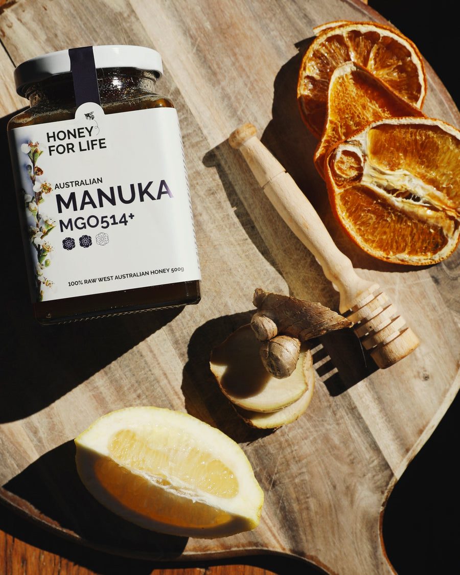 Manuka honey jar with honey dipper and lemon on a wooden board