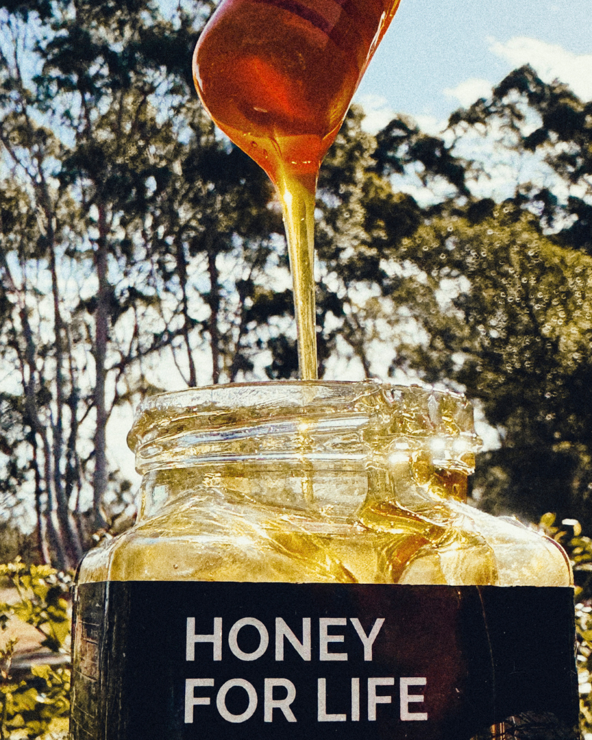 Honey being drizzled into a jar labeled 'Honey for Life' with a natural outdoor background.